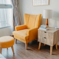 A yellow armchair and a stool next to a bedside table by a window