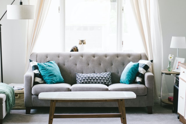 A gray sofa with pillows, next to a big window