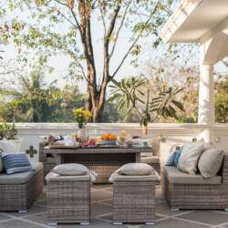 Outdoor patio with stools, couches, pillows, table covered in food, trees behind
