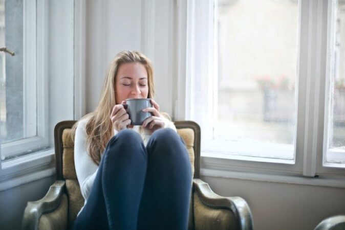 A girl is holding a mug while sitting in an armchair next to the window. Letting your furniture be directly exposed to the sunlight is not the smart way to extend the life of your furniture.
