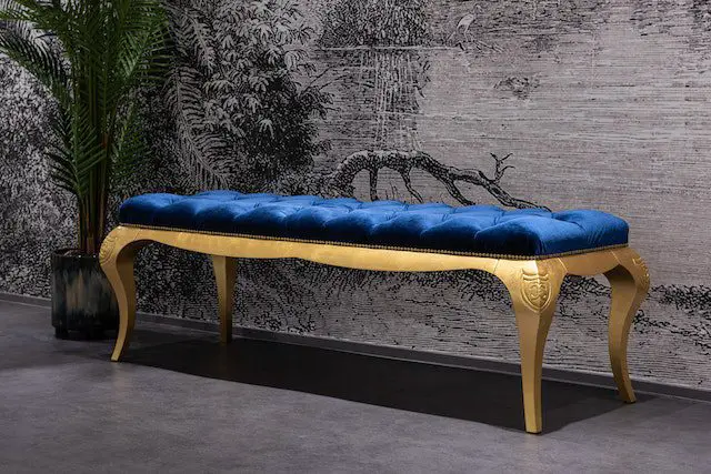 A blue bench with gold legs against a gray wall