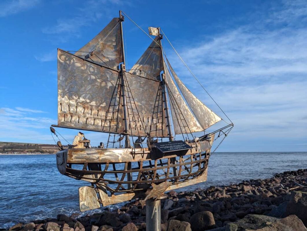 Metal ship sculpture by the sea with clear blue sky.