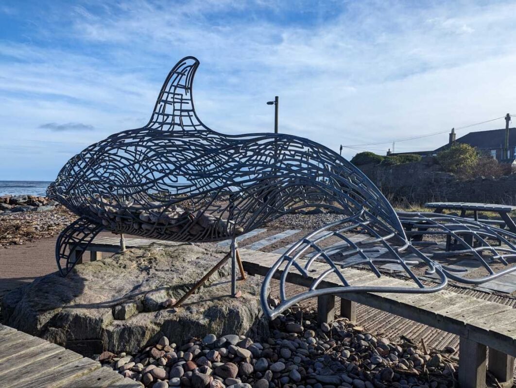 Metal whale sculpture by the beach.