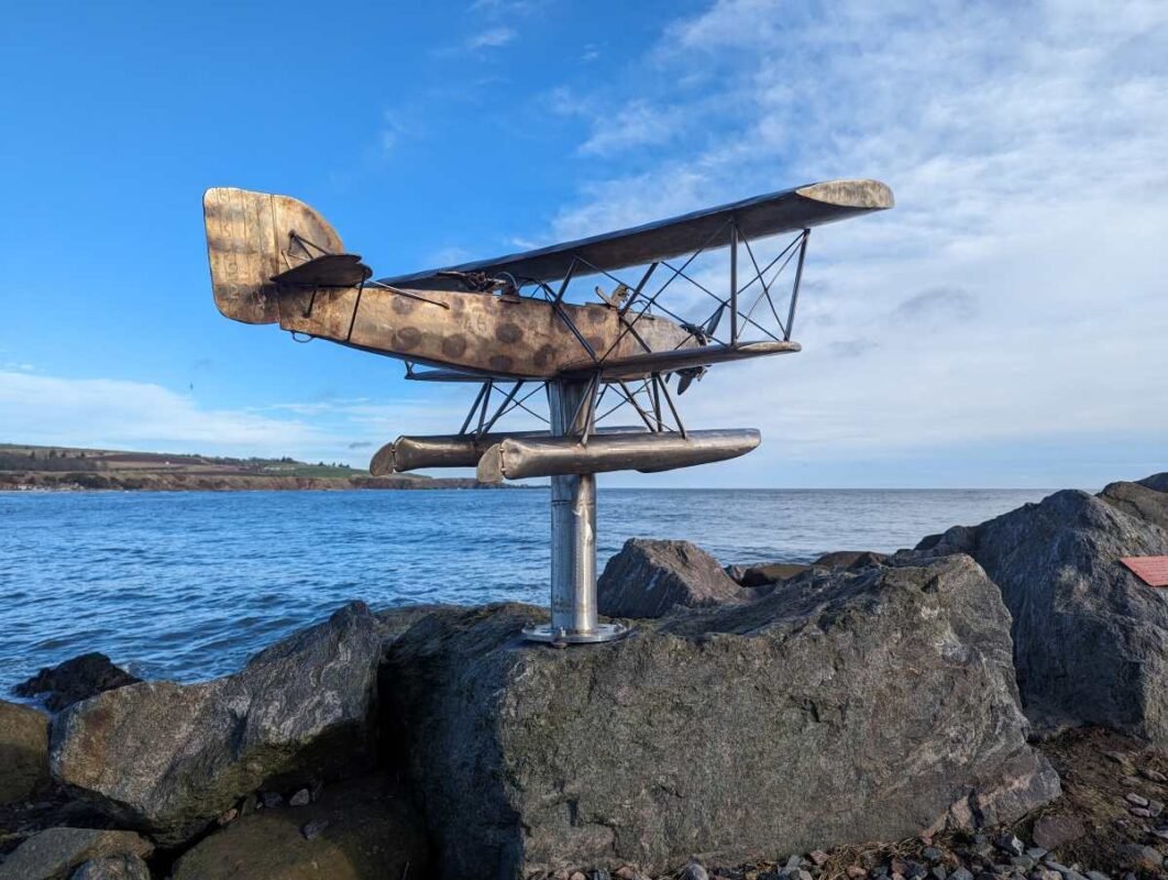 Seaplane sculpture on rocky shore with ocean background.