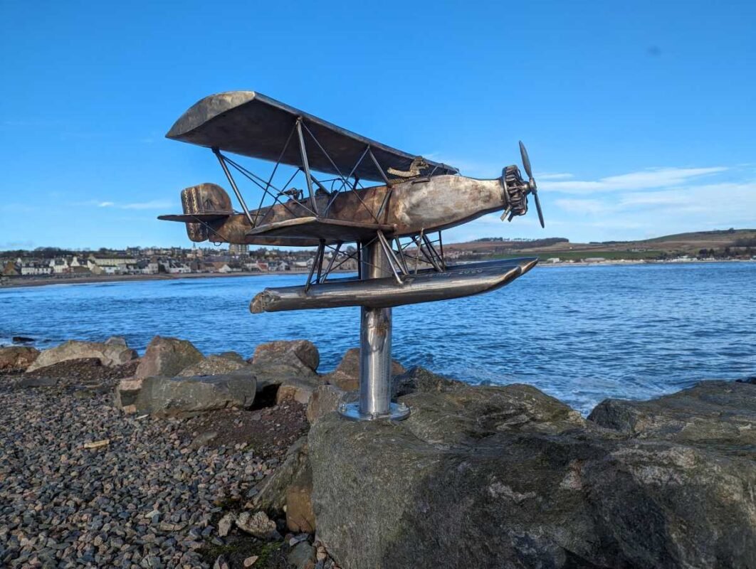 Vintage seaplane sculpture by the sea on rocky shore.